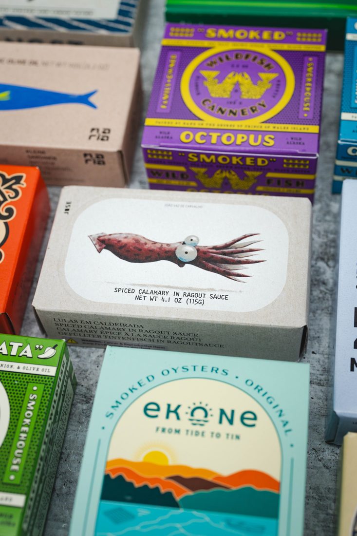 A colorful arrangement of tinned fish and smoked seafood including Wildfish Cannery octopus and Ekone oysters