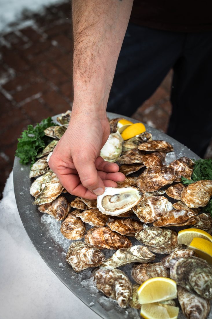 Hand reaching for an oyster on a platter dressed with lemon and parsley